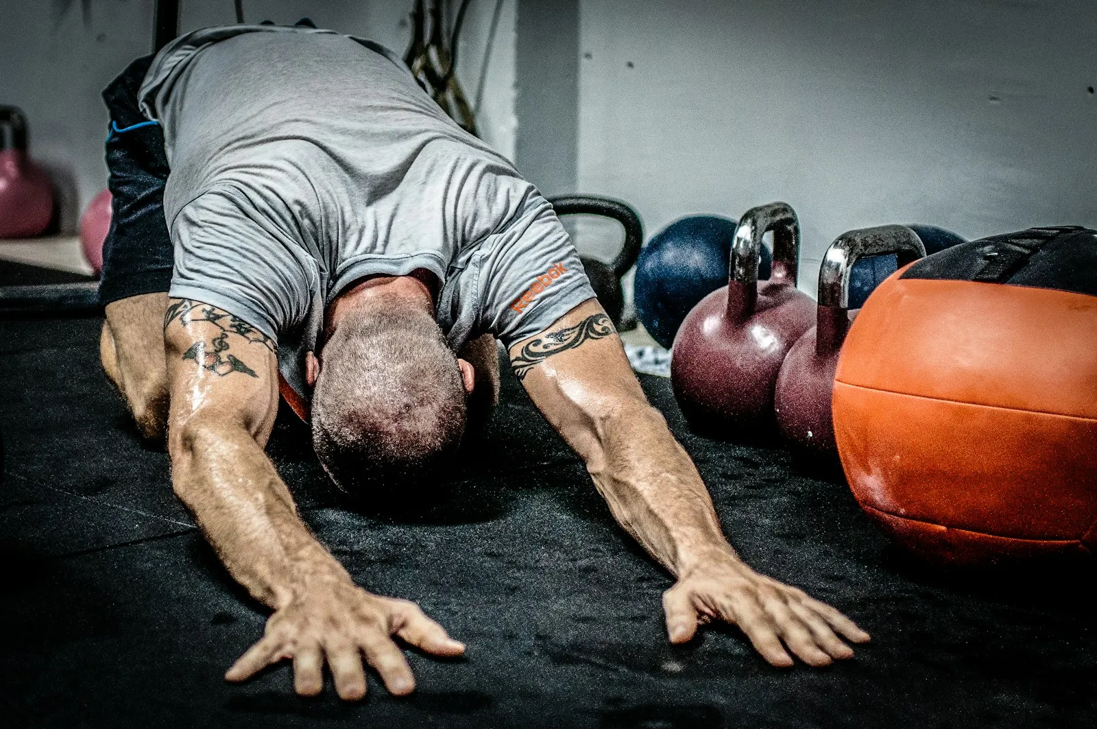 Atleta a alongar no chão de uma box de treino, junto a kettlebells e uma bola medicinal